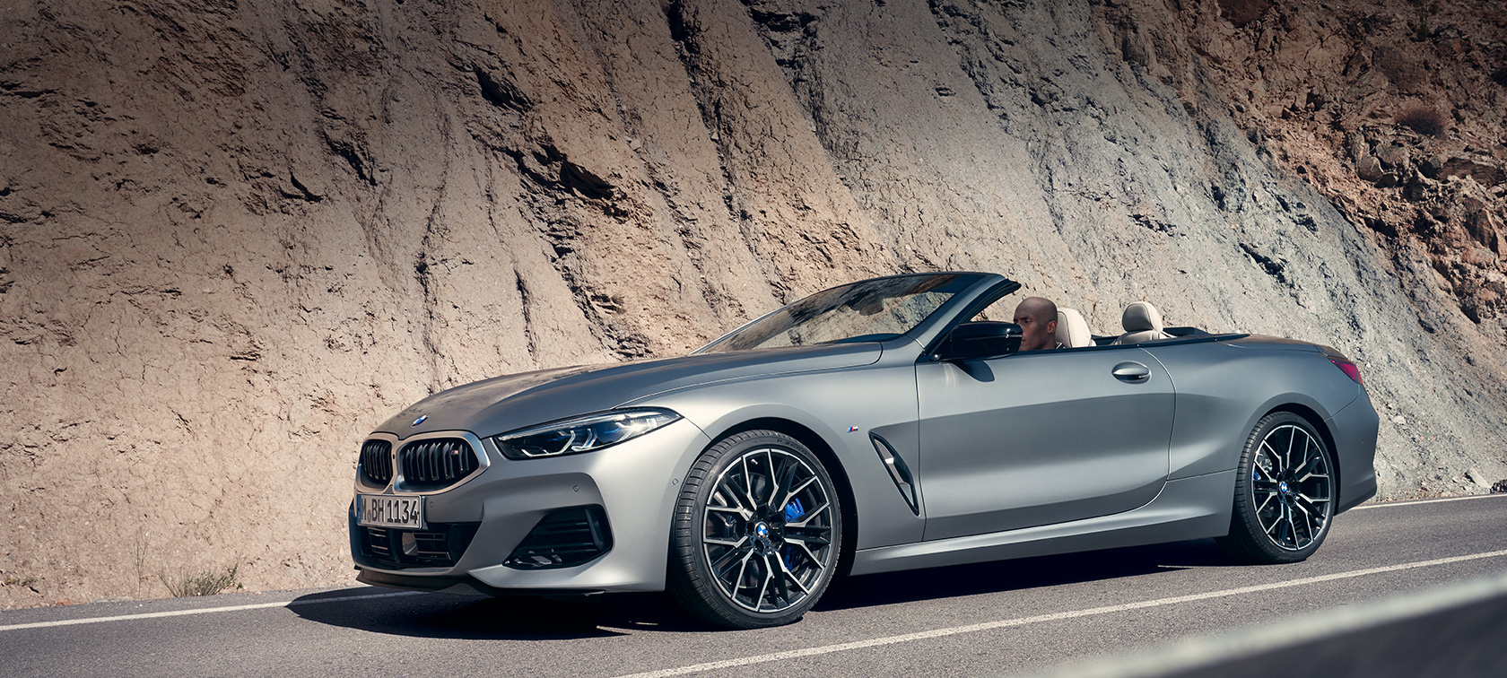 BMW 8 Series Convertible G14 LCI Facelift 2022 BMW Individual Frozen Pure Grey metallic side view with open softtop driving along mountain wall